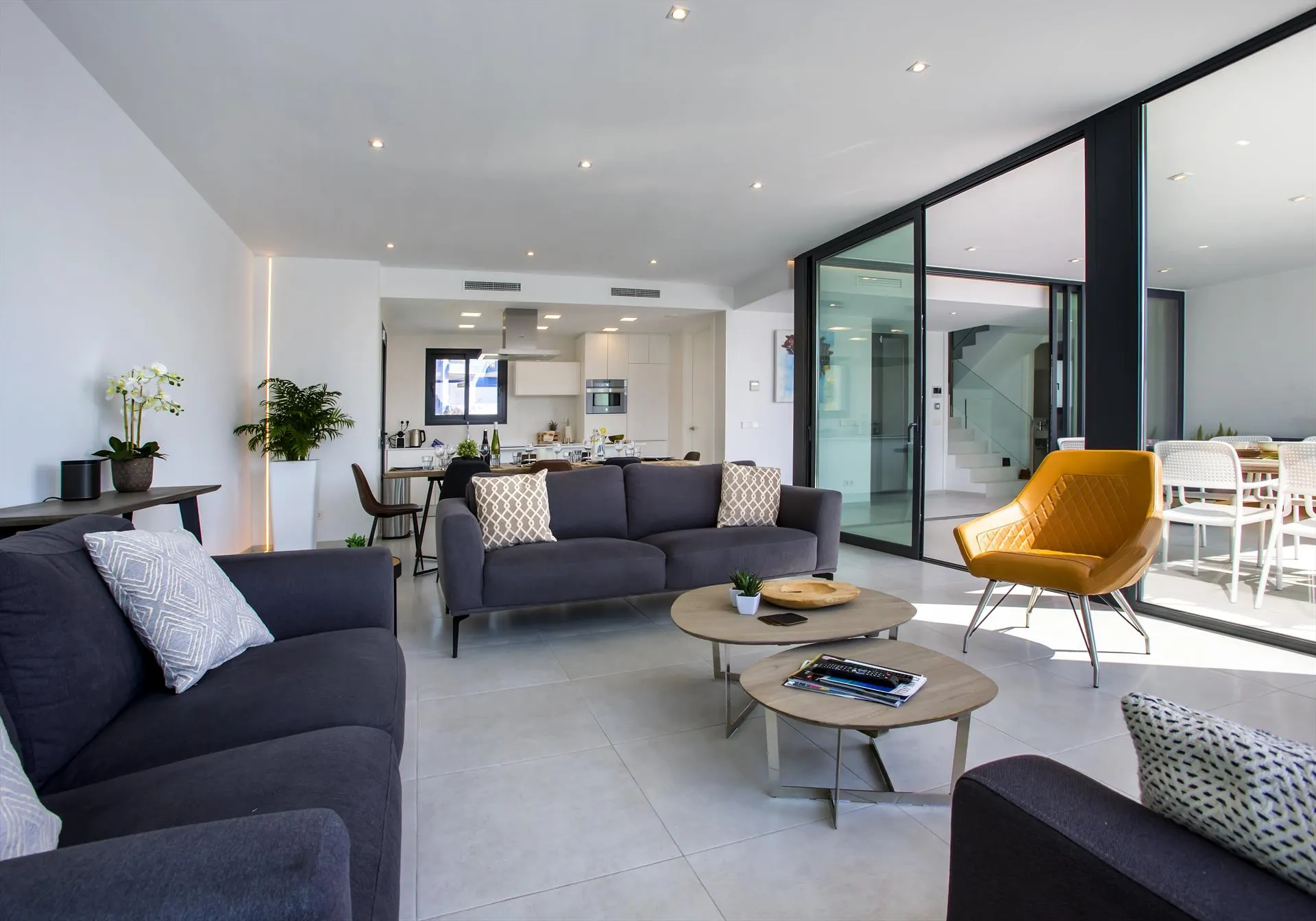 Das Wohnzimmer mit tiefem grauem Sofa, einem ockerfarbenen Sessel und zwei runden Tischen.