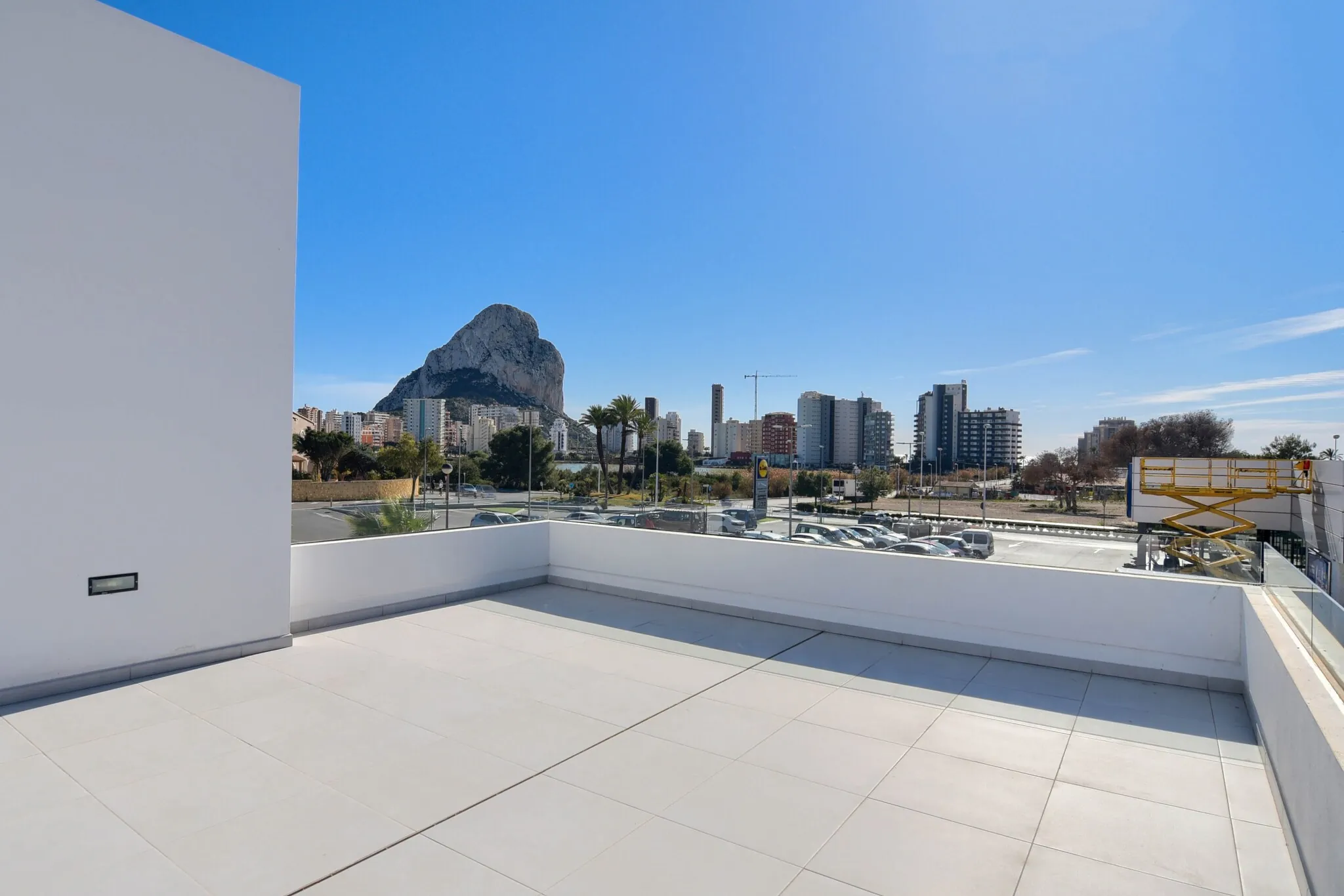 Die Dachterrasse: ein weiß gefliester Boden mit Brüstung, dahinter der Peñón de Ifach und die Skyline von Calpe.