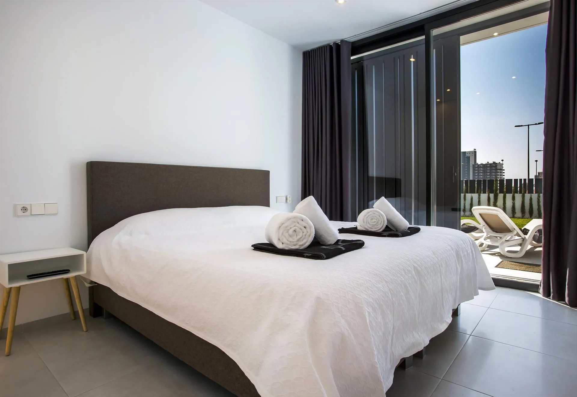 Ein Schlafzimmer mit Doppelbett, dunklem Kopfteil und Schiebetür zur Terrasse.